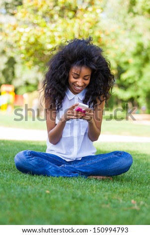Smiling teenage black girl using a phone, sitting on the grass - African people