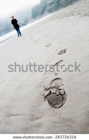 footprints on the beach sand on cloudy day and young woman walking on background
