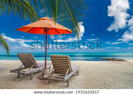 Beautiful tropical island scenery, two sun beds, loungers, umbrella under palm tree. White sand, sea view with horizon, idyllic blue sky, calmness and relaxation. Inspirational beach resort hotel