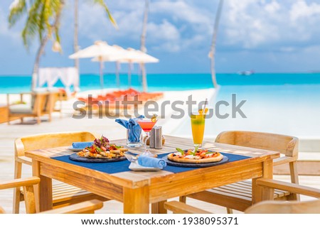 Luxury resort hotel poolside, outdoor restaurant on the beach, ocean and sky, tropical island cafe, tables, food. Summer vacation or holiday, family travel. Palm trees, infinity pool, cocktails, relax