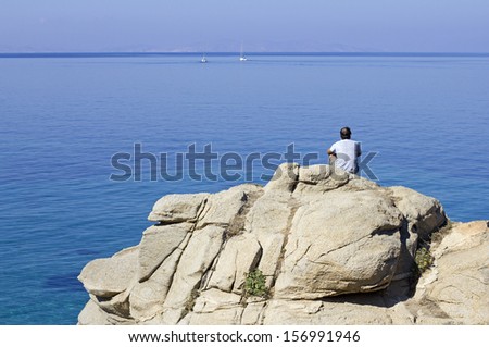 man looking at the sea on a big rock in mykonos island greece