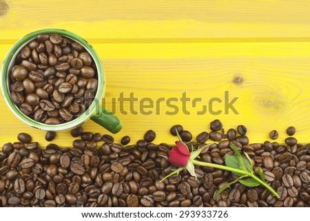 We love coffee. Roses resting on the coffee. Coffee beans, poured out on Yellow wooden table. Background for your text.