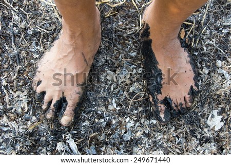 Bare feet above the muddy black men standing on hay burning ashes.