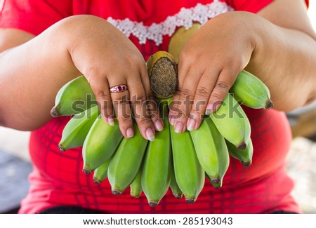 Close up of green bananas still raw in the hands of a fat woman wearing a red sweater.