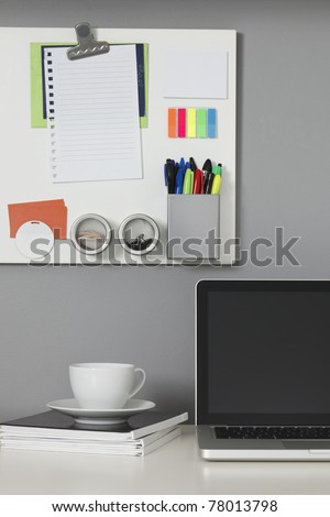 White office desk, laptop computer and a white magnetic board on a gray wall