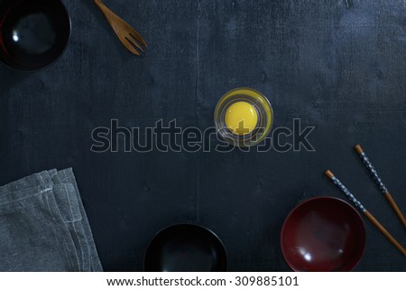 Black color wooden table top view. On the table are the Japanese wooden spoon, chopsticks, bowl,fresh raw eggs and table linen.