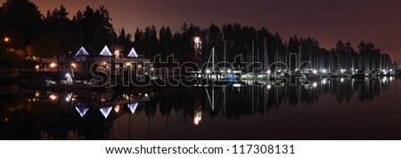 The Vancouver Rowing Club building and the adjacent marina at night reflect in the still water of Coal Harbor. The trees of Stanley Park silhouette in the background. British Columbia, Canada.