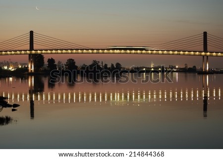 A rapid transit commuter train, crosses the Fraser River from Richmond into Vancouver. The train is a streak of light crossing the bridge due to the long exposure. British Columbia, Canada.