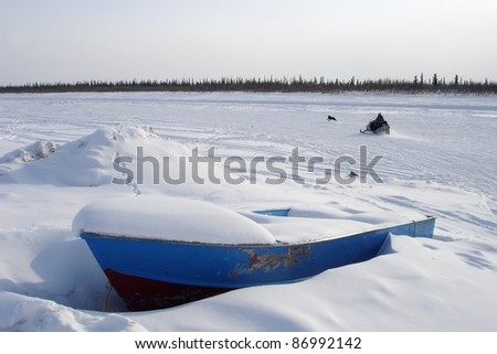 A snowmobiler and his dog, travel next to the winter ice road on the east channel of the Mackenzie River near Inuvik, Northwest Territories. A boat waits for the spring thaw.