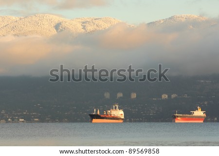 Freighters anchored in English Bay, Vancouver. Fresh snow blankets the Coast Mountains in the background. British Columbia, Canada.
