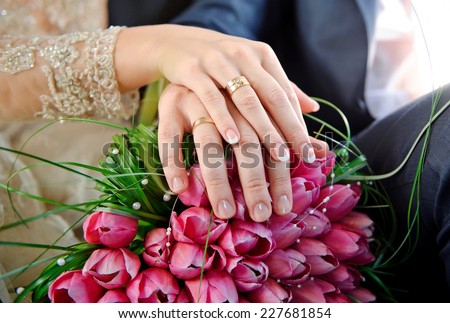 Hands with rings bride and groom on the wedding bouquet of pink tulips.