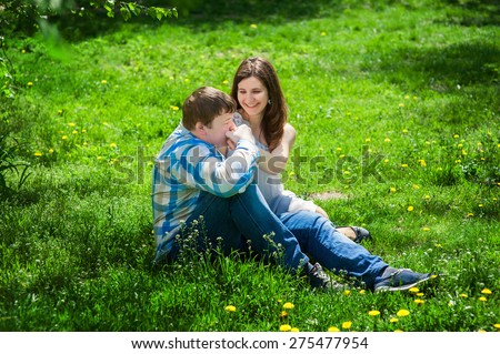 Man with a woman sitting on the grass and he kisses her hand.