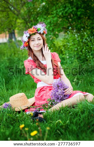 Beautiful woman in red dress sitting on the grass with a branch of lilac.