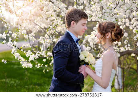Bride and groom look at each other in the blossoming spring garden.