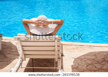 Woman in white hat lying on a lounger near the swimming pool.