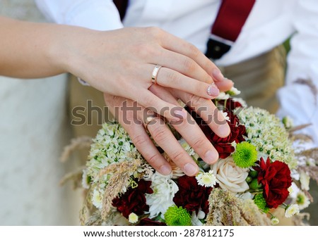 hands of the bride and groom with rings on wedding bouquet.