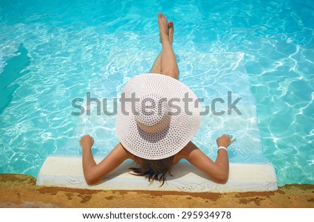 beautiful woman in a white hat sitting on the edge of the pool