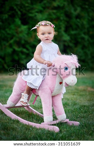 Little girl dressed up as cowgirl playing with toy horse in park.