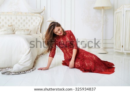 Beauty portrait of an attractive young woman laying in bedroom wearing a red dress and gently smiling