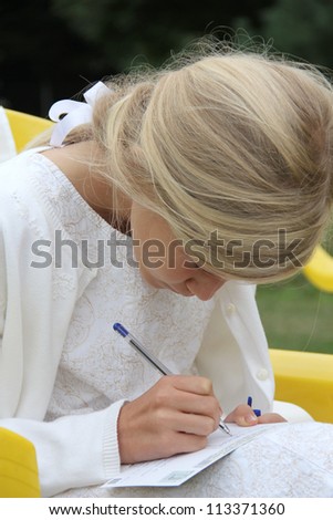 11-year old pretty blond girl in white dress, writing her best wishes on a card at a wedding