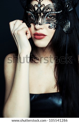 Portrait of a beautiful girl in a black dress with a theatrical mask on her face