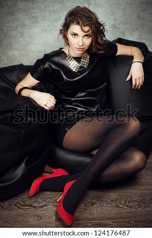beautiful woman posing in a studio in a leather dress and red shoes