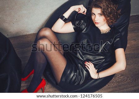 beautiful girl posing lying in the studio in the fashionable leather dress and red shoes.
