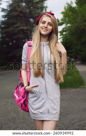 Portrait of a beautiful student walking through the park with a pink backpack. A girl wearing a bright beautiful hoop in the form of a bow