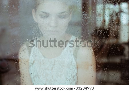 Attractive sad girl standing at the window watching the rain