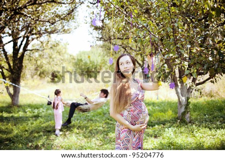 happy family playing on the lawn next to the hammock in the garden. Pregnant woman standing by a tree