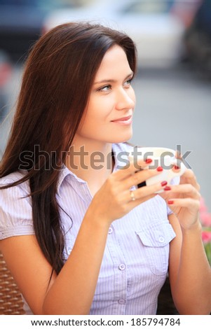 Woman drinking coffee and sitting outdoor, enjoying her morning coffee. Smiling happy female caucasian model in her 20s