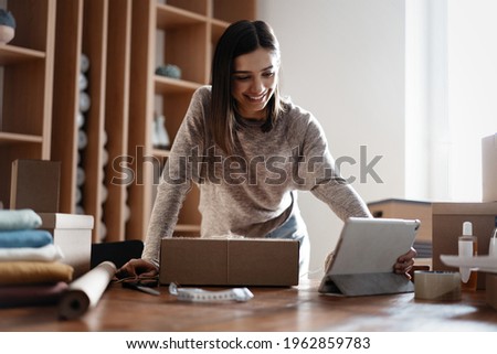 Indian mixed-race female seller using tablet checking ecommerce clothing store orders