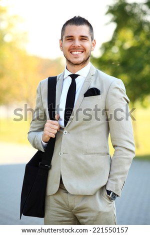 Young urban businessman running in street smiling wearing jacket and leather laptop bag on