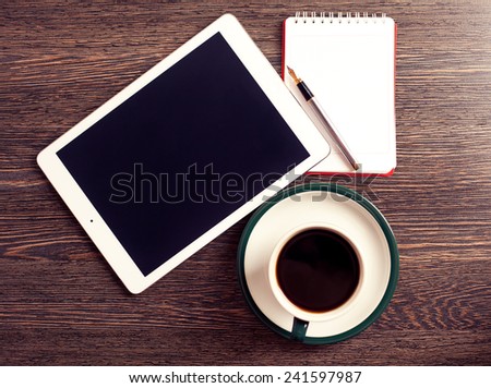 Digital tablet computer with cup of coffee on old wooden desk. Simple workspace or coffee break with web surfing