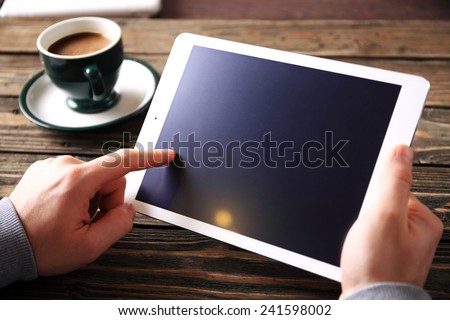 hands of a man holding blank tablet device over a wooden workspace table