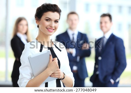 Business woman standing in foreground with a tablet in her hands, her co-workers discussing business matters in the background