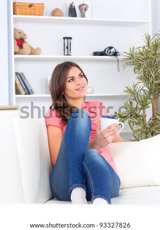 Pretty happy relaxed young lady sitting with coffee cup on couch