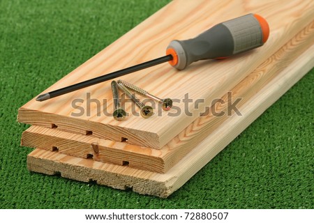 Three boards, screws and screw-driver lie on an artificial green lawn