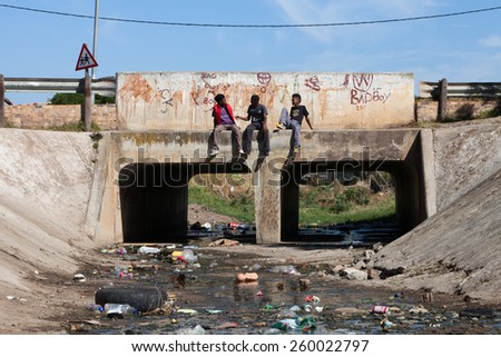 CAPE TOWN, SOUTH AFRICA - JANUARY 31: Three young township men sit and talk on a bridge with filthy water running underneath in a township, in Cape Town, South Africa, on January 31, 2012