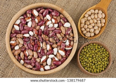 Assortment of legumes in wooden dishware on burlap: kidney beans, mung beans, chick peas