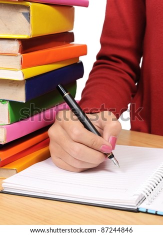 woman\'s hand writing with a pen beside a pile of books