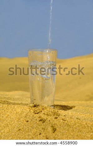 A glass of fresh water and bottle in a desert. Note that the water and bubbles are in motion blur.