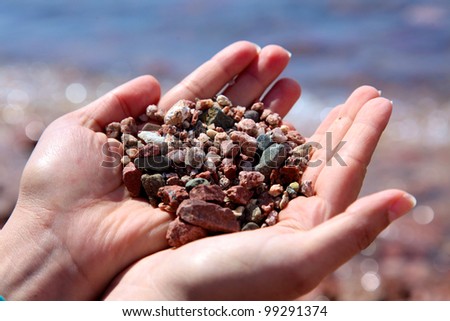 Hands holding stones & pebbles at beach on a blurry background