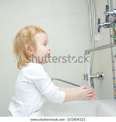 The little blonde happy smiling girl washing hands and face with soap in the bathroom. Hygiene. The girl wearing a blank white shirt. Ready for your design or logo