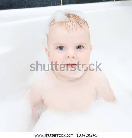 Cute baby boy with blond hair and blue eyes is washing hair hair and body i in bath. The symbol of purity and hygiene education