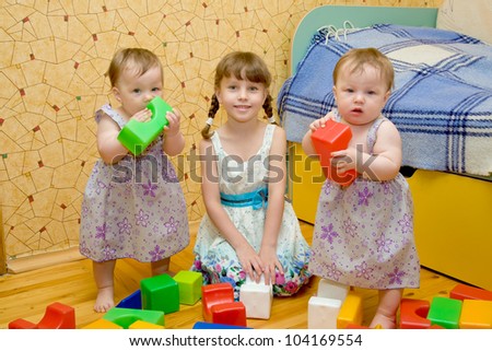 Three sisters - a  preschooler girl and two twins baby toy building of the blocks. Older sister teaching younger.