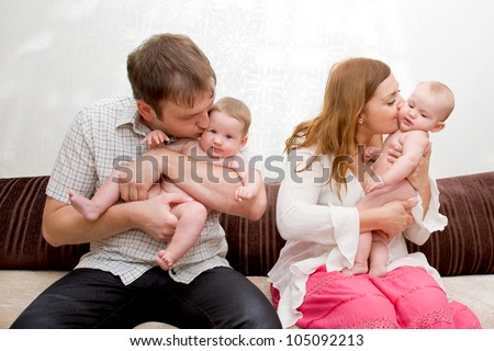 Happy mother and father kissing and laughing with two tiny babies twin sisters girls. Big Family