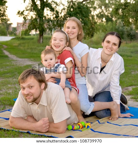 Big family - smiling father, mother and three daughters on the green grass in the park. Happy family concept