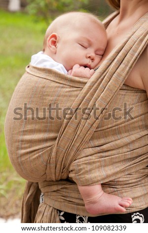 Best deep sleep. Newborn baby sleeping in a sling, in the embrace of her mother.