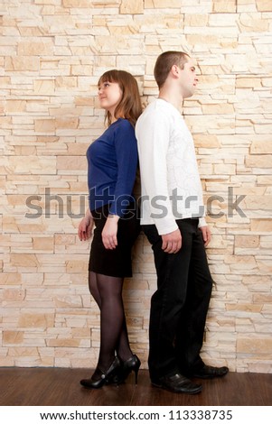 Young couple - a boy and girl standing back to back against a brick wall. Quarrel, dispute, compromise search